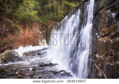 A Waterfall Flowing Over A Stone Wall At Burr Pond Torrington, Connecticut In Wintertime.