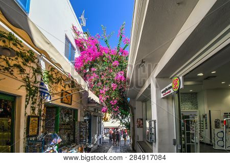Santorini, Greece - September 16 2018: A Colorful, Narrow Street With Souvenir Shops And Pink Bloome