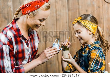 Happy Mother Watering Small Plant With Toy Watering Can Near Cute Daughter