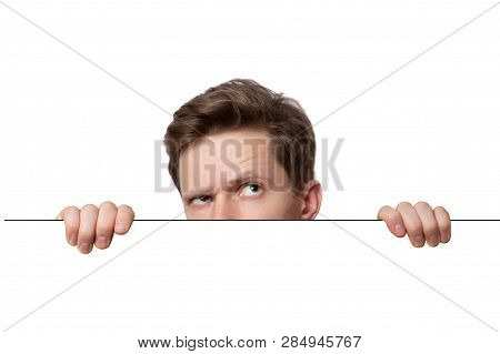 Young Man With Surprised Eyes Peeking Out From Behind Billboard Paper Poster. Funny Man Peeking Out 