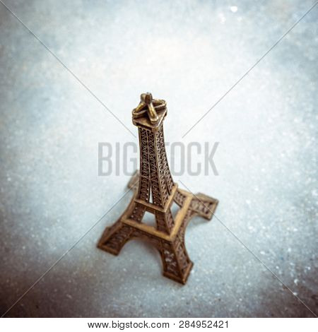 Souvenir model of the Eiffel Tower on cement floor. Strong vignette, split toning effect and film grain filters.
