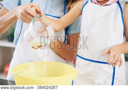 Close-up Image Of Mother And Daughter Pouring Fresh Cold Cream In Bowl When Making Sweet Frosting
