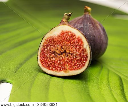 Ripe Juicy Purple Figs On A Green Leaf Background. Top View. One Fruit In Its Entirety, The Other Ph