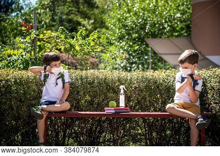 Coronavirus School Reopening Concept: A School Boys Sit On Bench In Front Of A School Wearing A Face