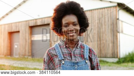 Portrait Of Beautiful African American Young Woman Farmer Standing In Field At Shed On Background An