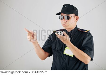 Serious Policeman In Sunglasses Using Walkie-talkie Or Police Radio During Demonstration And Contoll