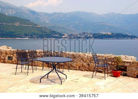 เก้าอี้เหล็กสีน้ำเงินและตารางบนระเบียงหินวิวทะเล