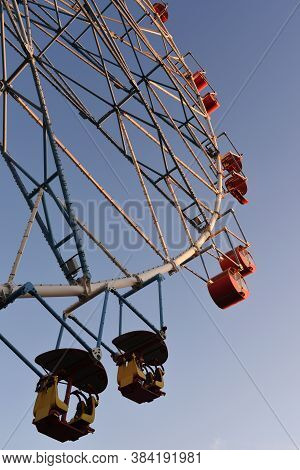 A Part Of White Ferris Wheel With Colorful Cabins Against The Backgroud Of The Blue Sky With Clouds.