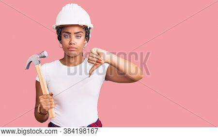 Young african american woman with braids wearing hardhat holding hammer with angry face, negative sign showing dislike with thumbs down, rejection concept 