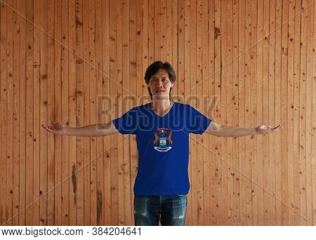 Man Wearing Michigan Flag Color Shirt And Standing With Arms Wide Open On The Wooden Wall Background