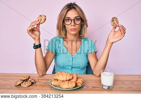 Beautiful caucasian woman sitting on the table eating breakfast relaxed with serious expression on face. simple and natural looking at the camera. 