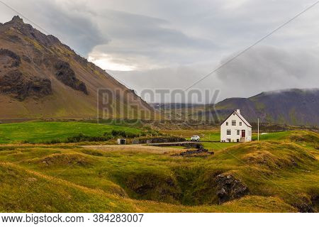 Arnarstapi, Iceland- 26 August 2015: A White Traditional House In A Small Town. Mountains Around.