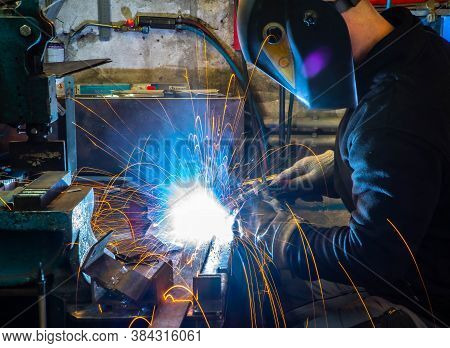 Electric Welding Process. Worker In Welding Mask. Yellow Sparks Fly To The Sides. Bright White.