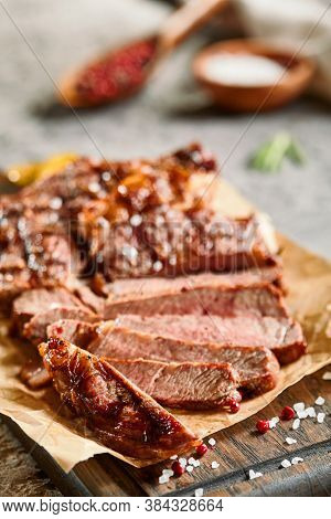 Classic ribeye steak served in waxed paper on wooden cutting board. Cut against grain beef steak. Roasted beef steak with yellow chilli pepper slices and salt crumbs. Rustic spoon and spice bowl