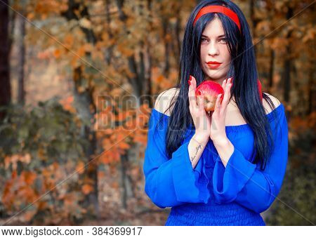 Modern Snow White In Blue Dress Holds An Apple In The Woods. Snow White Princess With The Famous Red