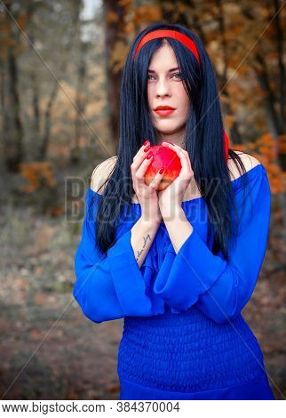 Modern Snow White In Blue Dress Holds An Apple In The Woods. Snow White Princess With The Famous Red