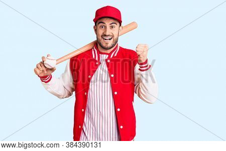 Young handsome man holding baseball bat and ball screaming proud, celebrating victory and success very excited with raised arms 