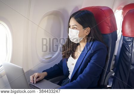 A Young Businesswoman Wearing Face Mask Is Using Laptop Onboard, New Normal Travel After Covid-19 Pa