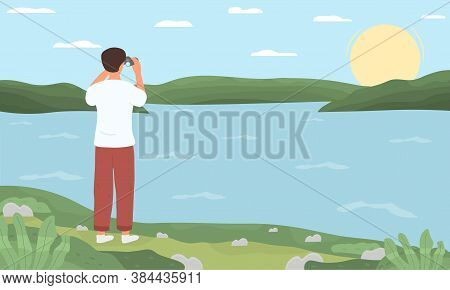 A Young Man Standing On The Shore Of A Lake Or River And Looking At The Horizon With Binoculars. Fla