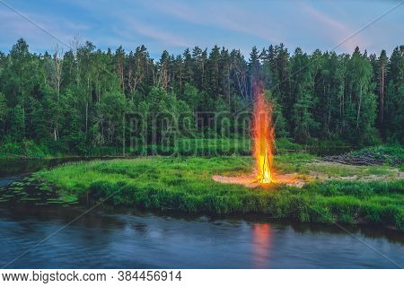 Traditional Midsummer Ligo Celebration. Huge Bonfire On The River Shore. Scenic Landscape Of Forest 