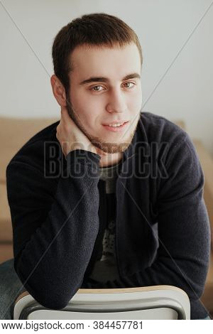 Handsome Man Wearing A Black Jacket And Jeans Sitting Down Intside
