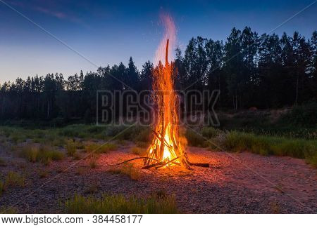 Traditional Midsummer Ligo Celebration In Latvia. Huge Bonfire. Scenic Landscape Of Forest At Twilig