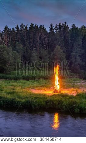 Landscape Of Forest And River At White Night. Huge Bonfirefire. Midsummer Ligo Celebration In Latvia