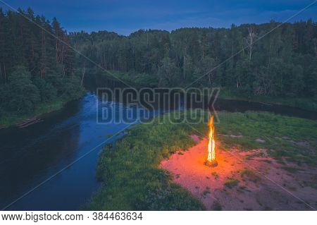 Midsummer Ligo Celebration. Drone View Of Huge Fire On The River Shore. Scenic Landscape Of Forest A