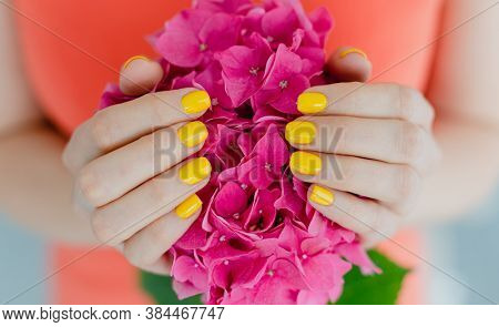 Women with manicured nails in yellow holding a flower
