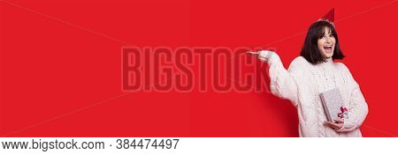 Brunette Lady Advertising Something Holding On Her Palm On A Red Studio Wall With A Gift In Hand And