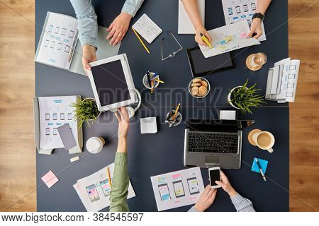 business, people and team work concept - team of startuppers with gadgets and papers working at office table