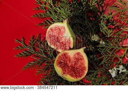 Fig Halves On A Red Background With A Plant. Fig Slices With Thuja.