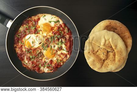 Shakshuka - Poached Eggs In Tomato Sauce, Onion, Pepper And In Iron Pan With Pita Bread On Dark Wood