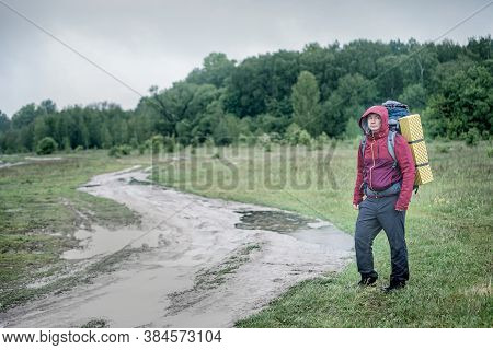 Guy Tourist Hiker Walks Along The Road With A Backpack In A Red Jacket In The Rain