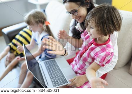 Woman Is Sitting On The Couch, Girl Is Sitting On Her Lap, They Are Looking At Laptop Next To Childr
