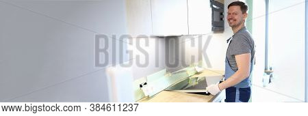 Portrait Of Cheerful Handyman Setting Cookstove On Kitchen. Professional Service Worker In Uniform H