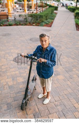 Active Old Woman Riding Electric Scooter. Retired Lady Uses Environmentally Friendly City Vehicle. G
