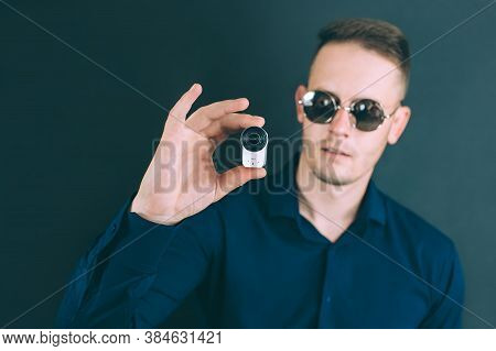 The Guy Takes Photos, Videos With An Action Camera, With One Hand. On A Black Background In The Stud