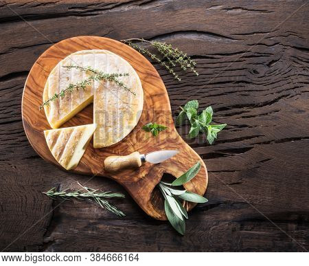 Head of brie cheese or raclette cheese with herbs on wooden table. Top view.