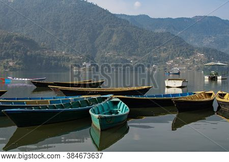 View Over A Few Colorful Boats On Phewa Lake In Pokhara, Nepal With The Surrounding Mountains In The