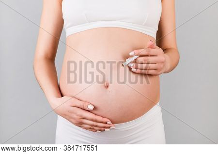 Close Up Of Pregnant Woman In White Underwear With A Cigarette Against Her Belly At Gray Background.