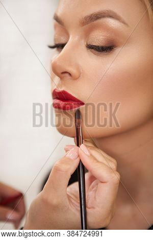 Vertical Shot Of A Makeup Artist Applying Red Lipstick On The Lips Of A Female Client