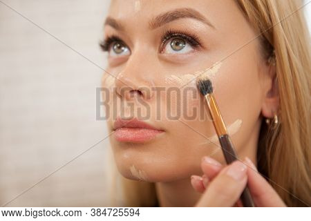 Close Up Of A Makeup Artist Applying Liquid Concealer Or Highlighter On The Face Of Female Client