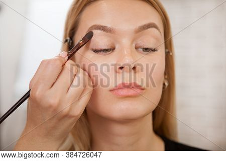 Professional Makeup Artist Applying Eyeshadow Base On Eyelids Of A Female Client