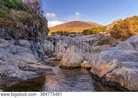 Mountain Stream Flowing Between Rocks With Mountain Peak Of Slieve Donard, Highlighted By Sunlight I