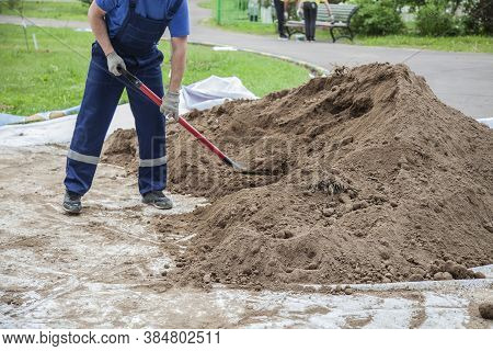 The Gardener Sprinkles A Flower Bed With A Shovel. Creation Of Landscape Design In The Garden. The M