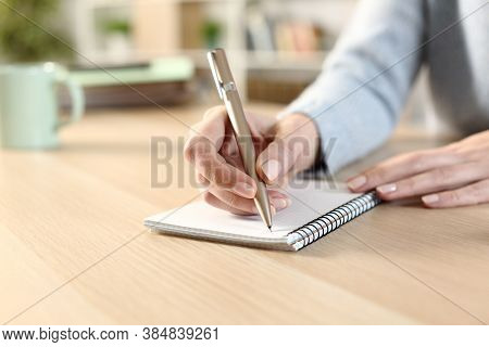 Close Up Of A Woman Hand Witing On A Notepad Sitting On A Desk At Home