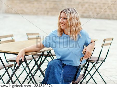 Young Women Wearing T-shirt And Jeans Sits In A Street  Cafe