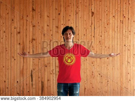 Man Wearing Kyrgyzstan Flag Color Shirt And Standing With Arms Wide Open On The Wooden Wall Backgrou