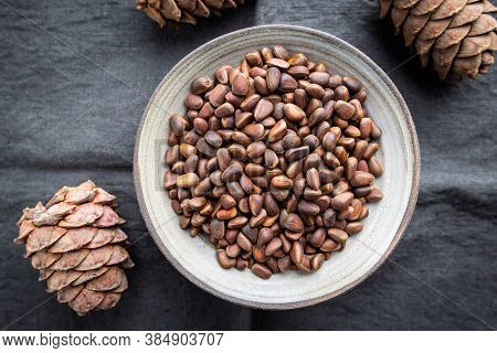Cedar Or Pine Nuts In A Bowl With Cones On Gray Background, Top View